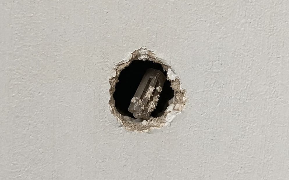 Torn drywall anchor hole with the old plastic anchor still inside the wall