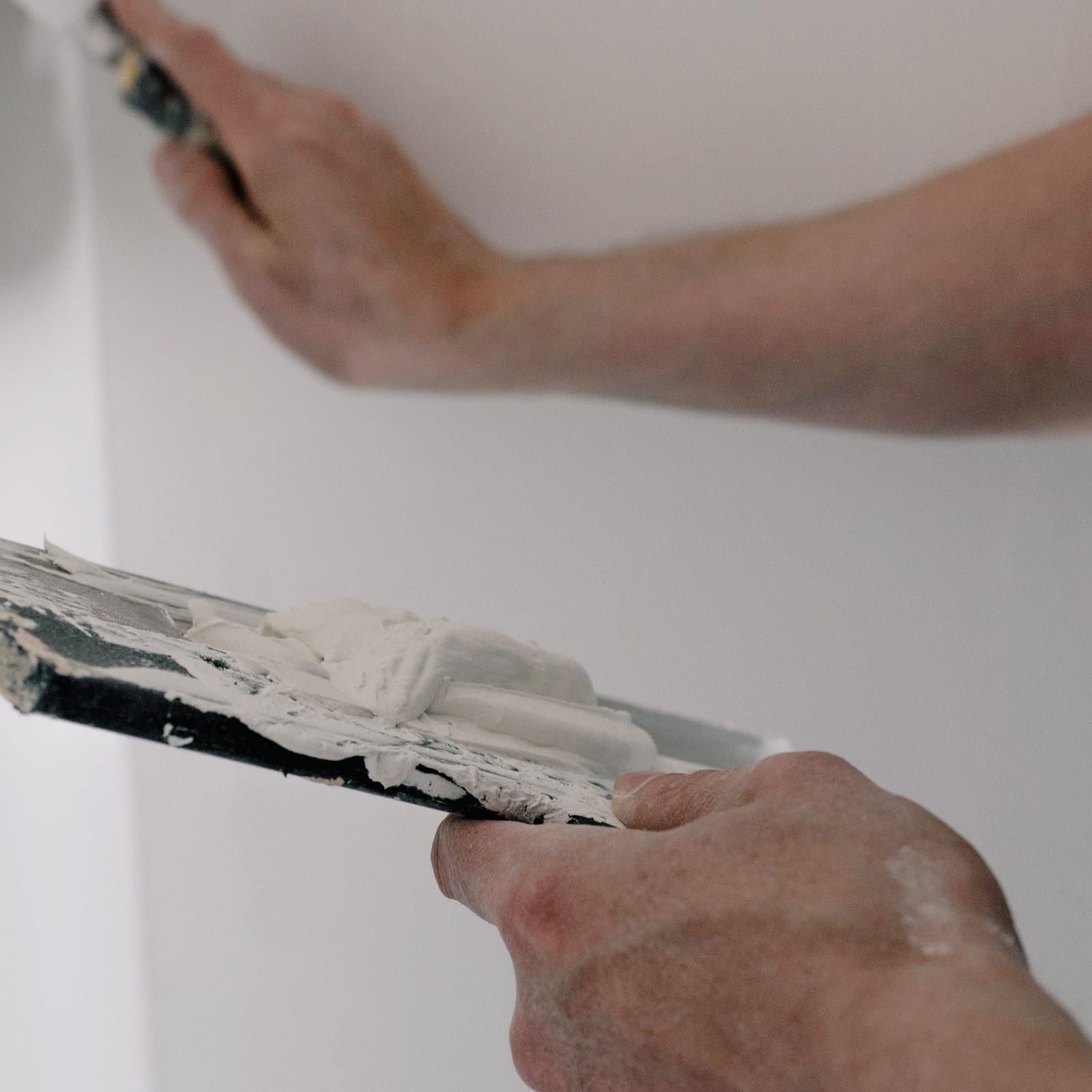 Joint compound being skimmed flat across a repaired section of wall