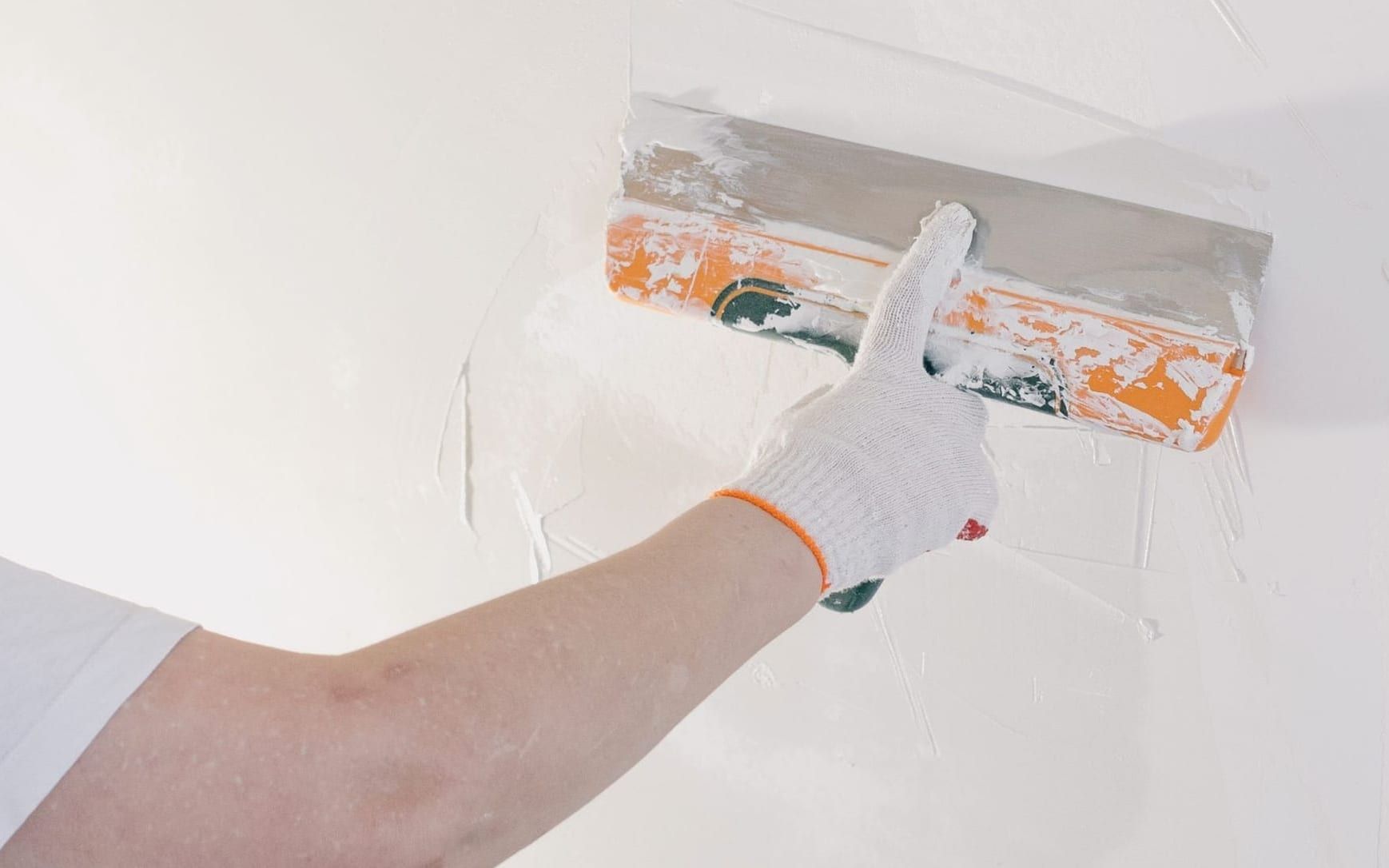 Wide knife skimming joint compound flat across a patched section of wall