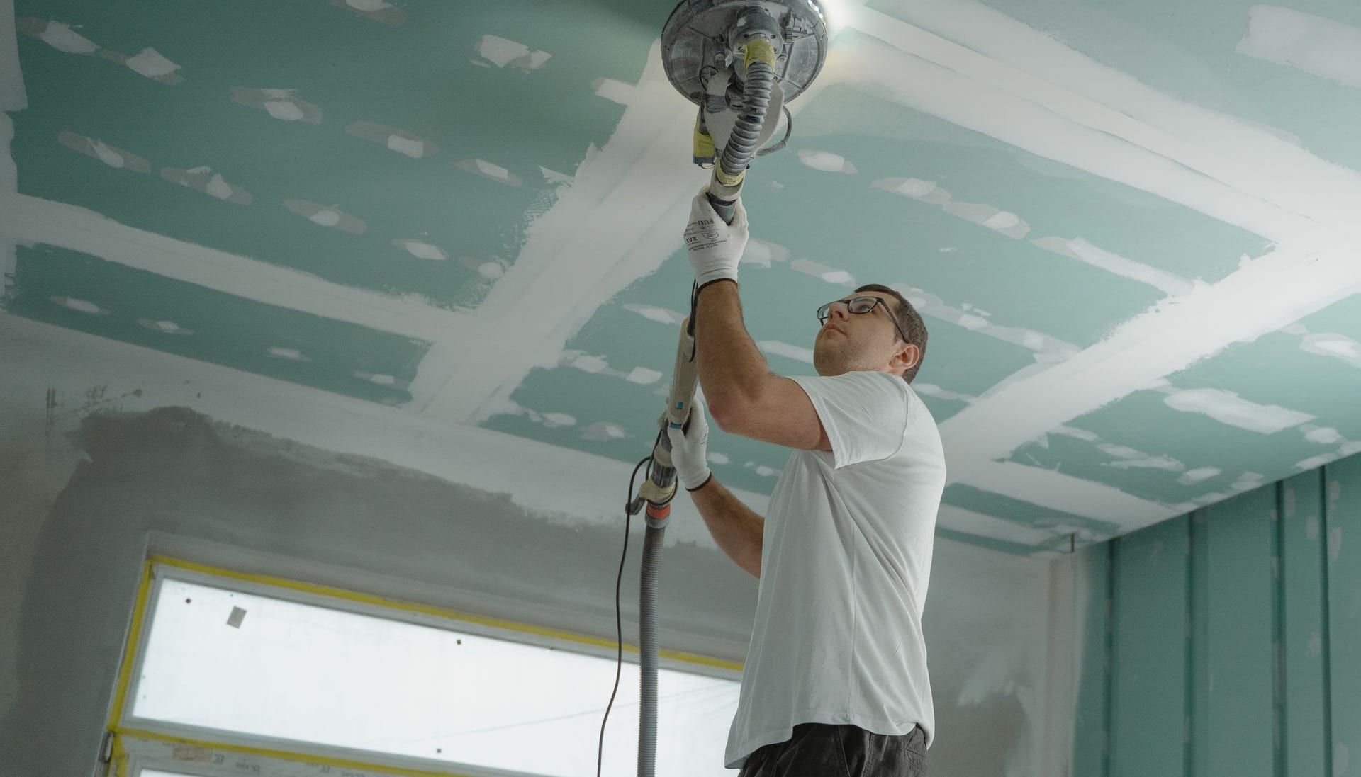 Contractor sanding a drywall ceiling joint during a repair