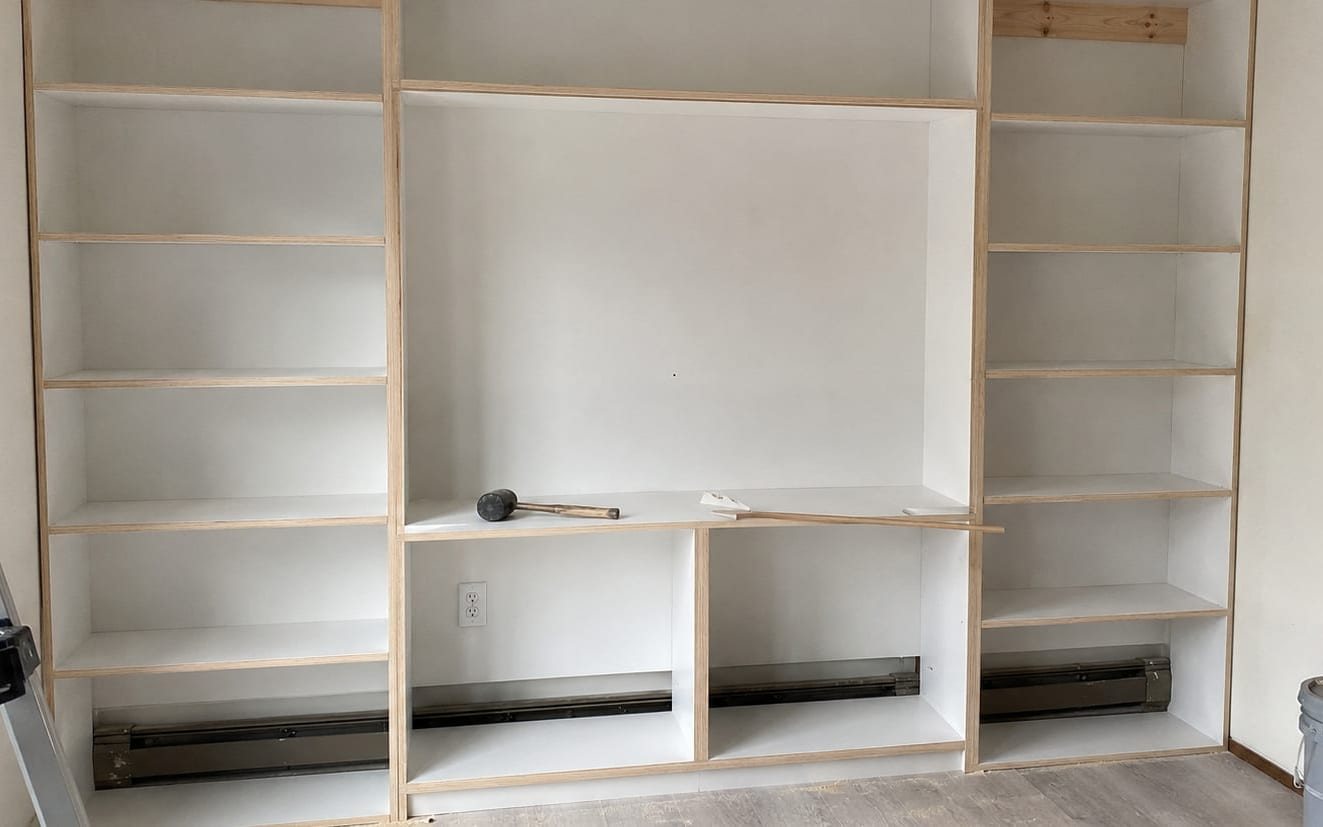 Built-in wall shelving unit mid-assembly with a mallet resting on one shelf