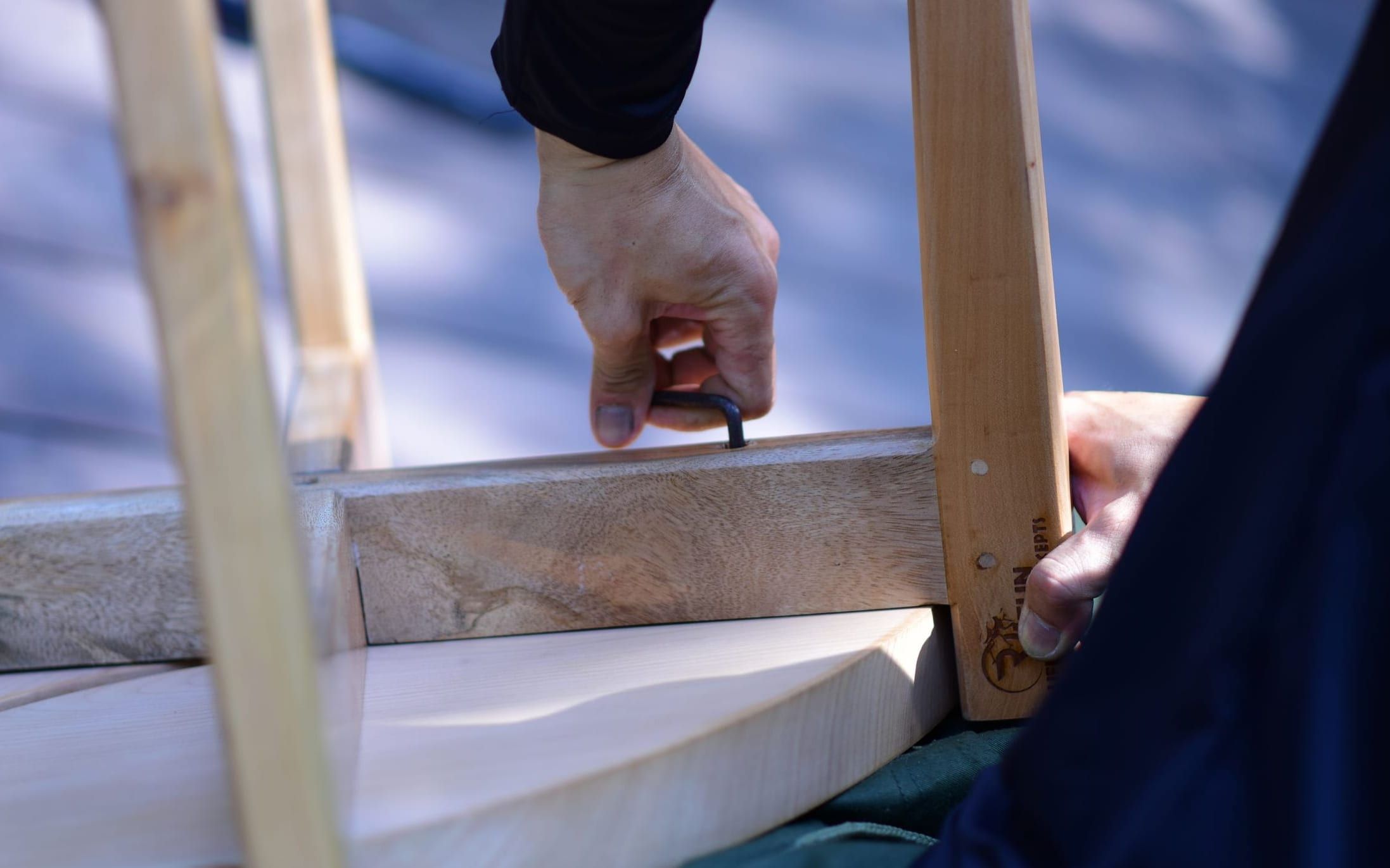 Hands driving a fixing into a wooden table frame during assembly