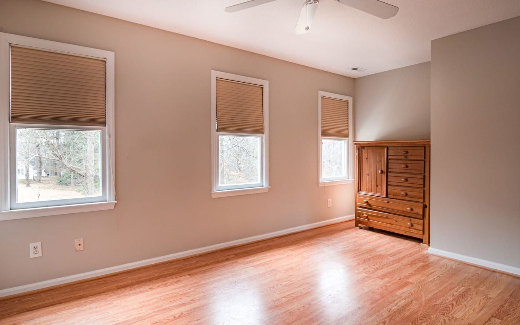 Cleared bedroom with wood floors and a single dresser left against the far wall