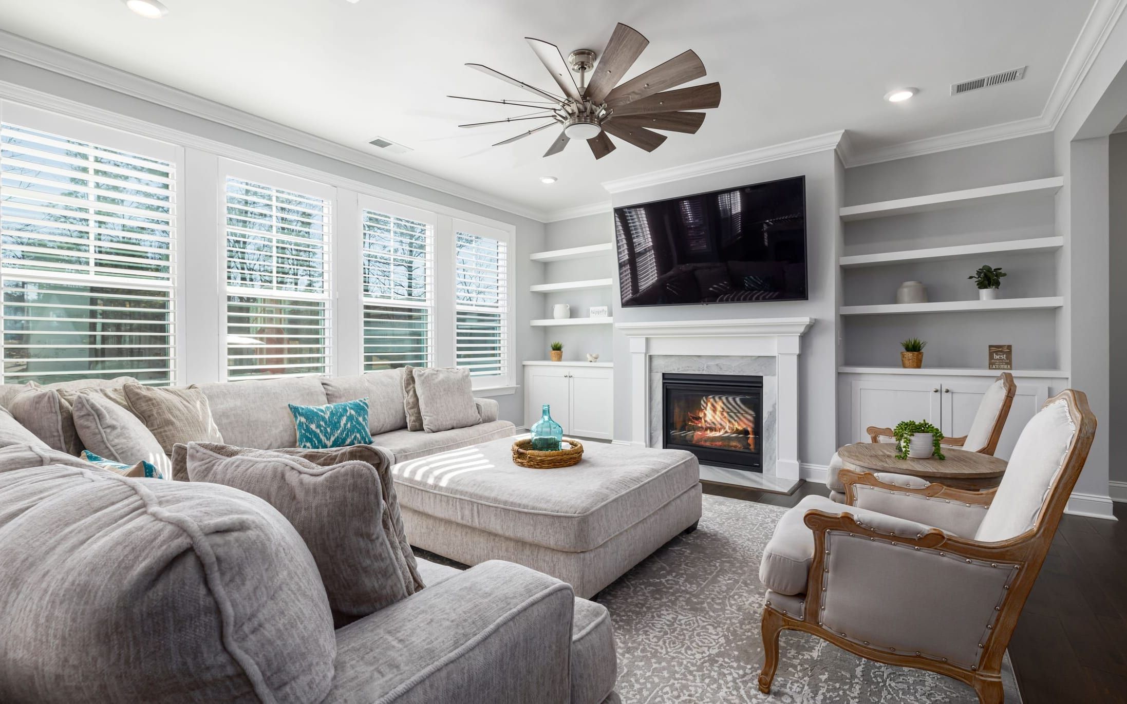 Family room with a TV mounted above the fireplace between white built-in shelves