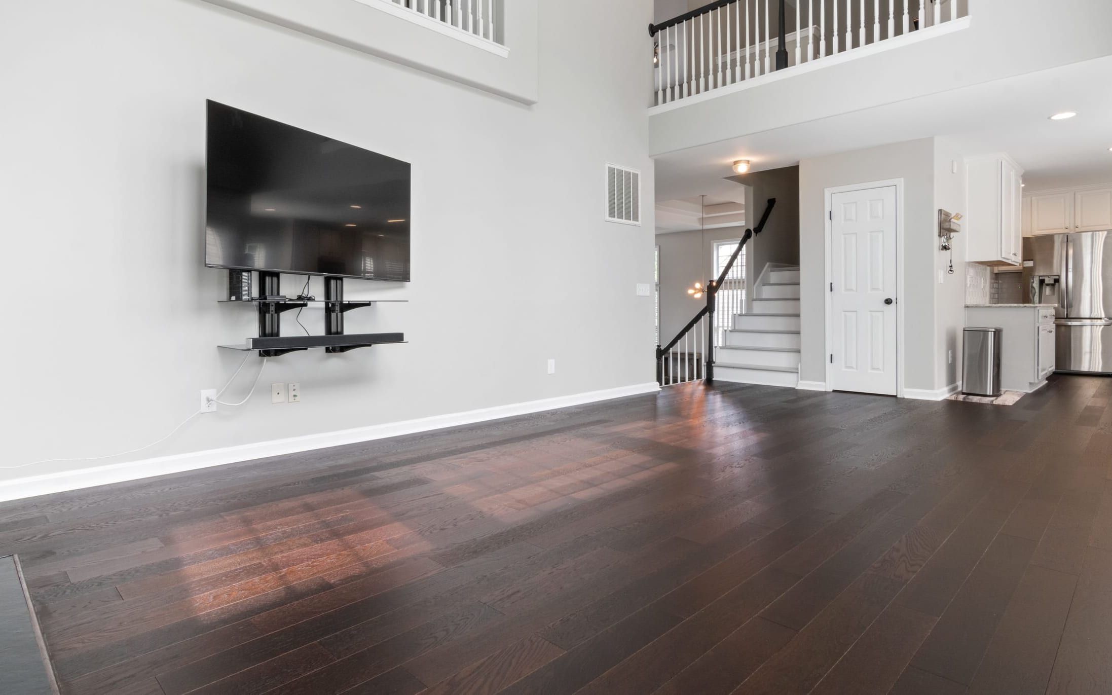 TV mounted high on the wall of an open two-storey living room with dark wood floors