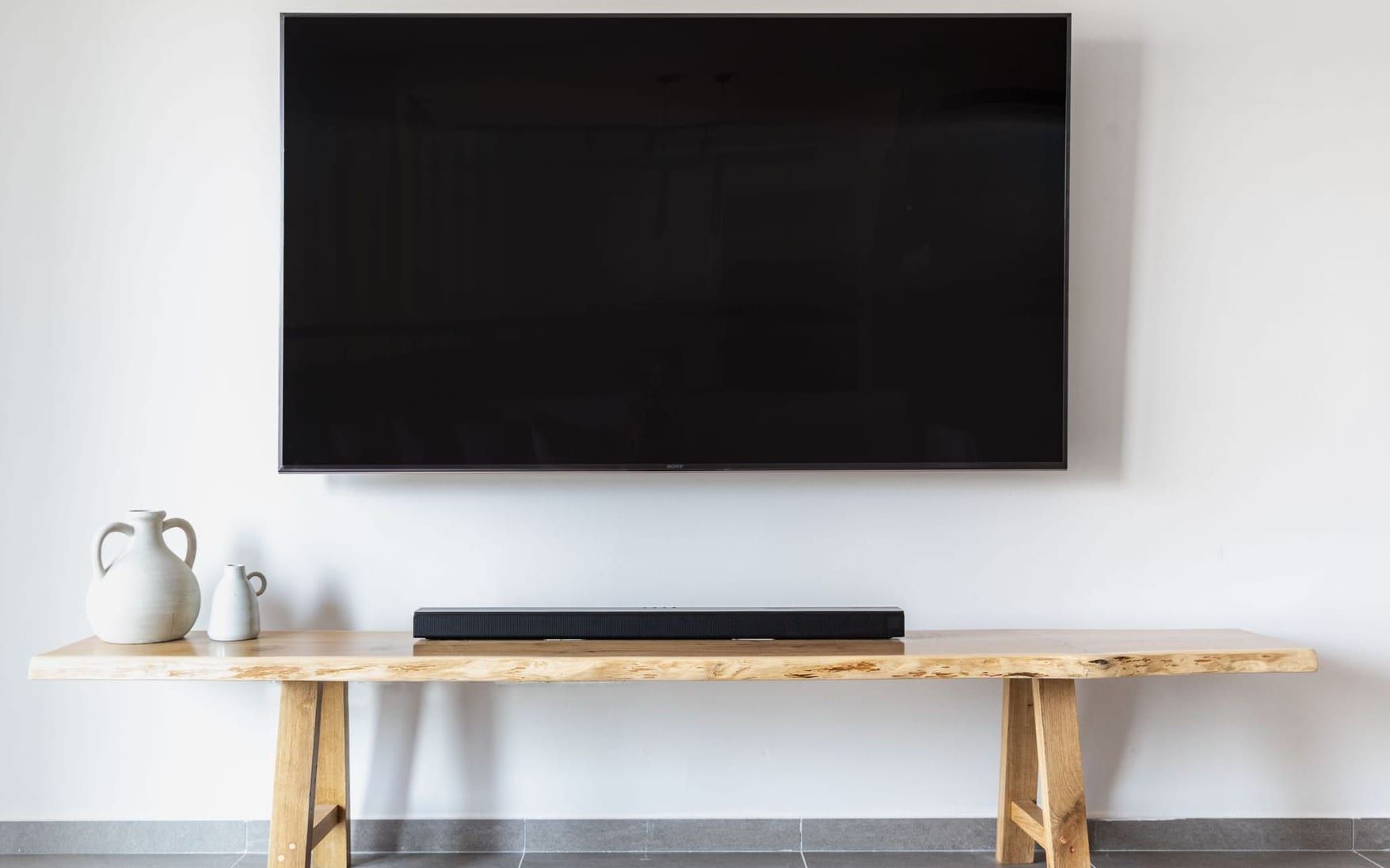Flat-screen TV with a soundbar mounted on a clean white wall above a wooden console