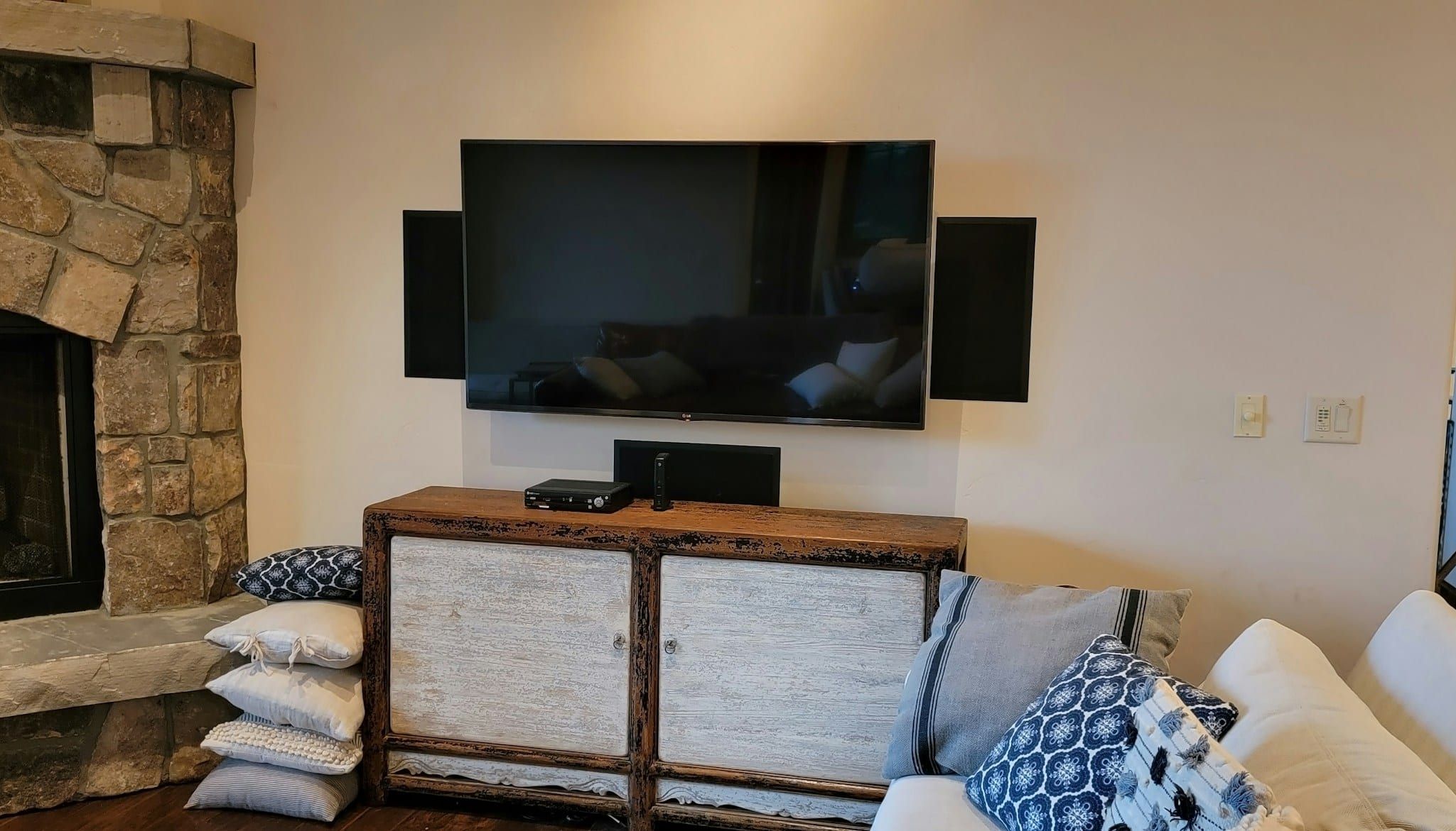 Large TV and speakers mounted on a stone accent wall above a media console